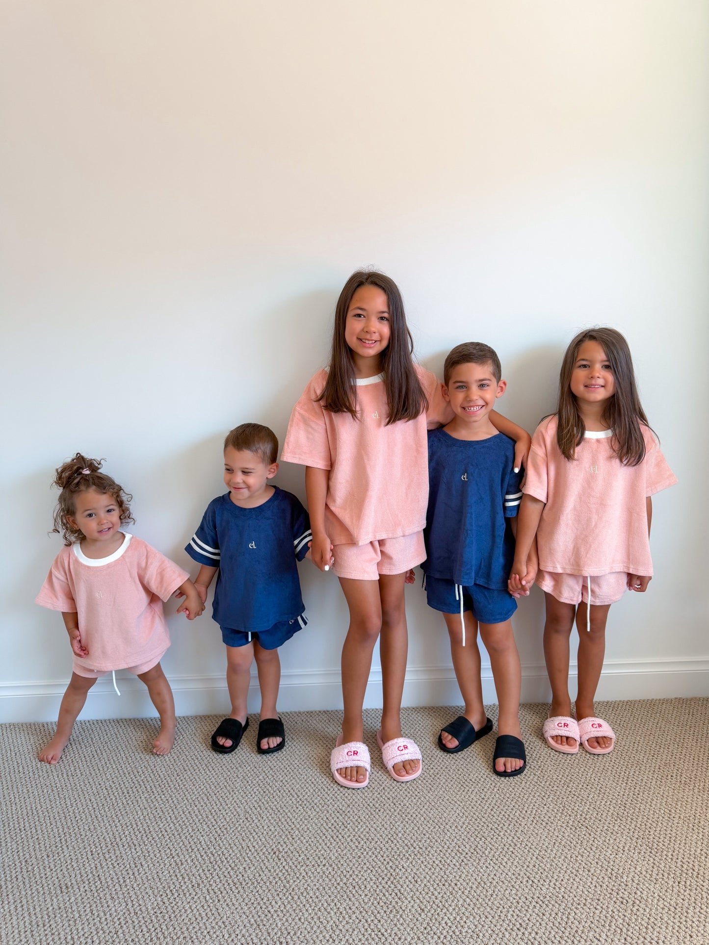 Five children wearing matching outfits standing against a white wall.