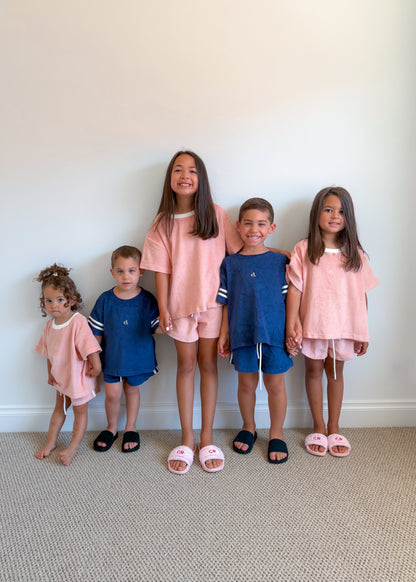 Five children standing in a row wearing matching outfits against a plain wall.