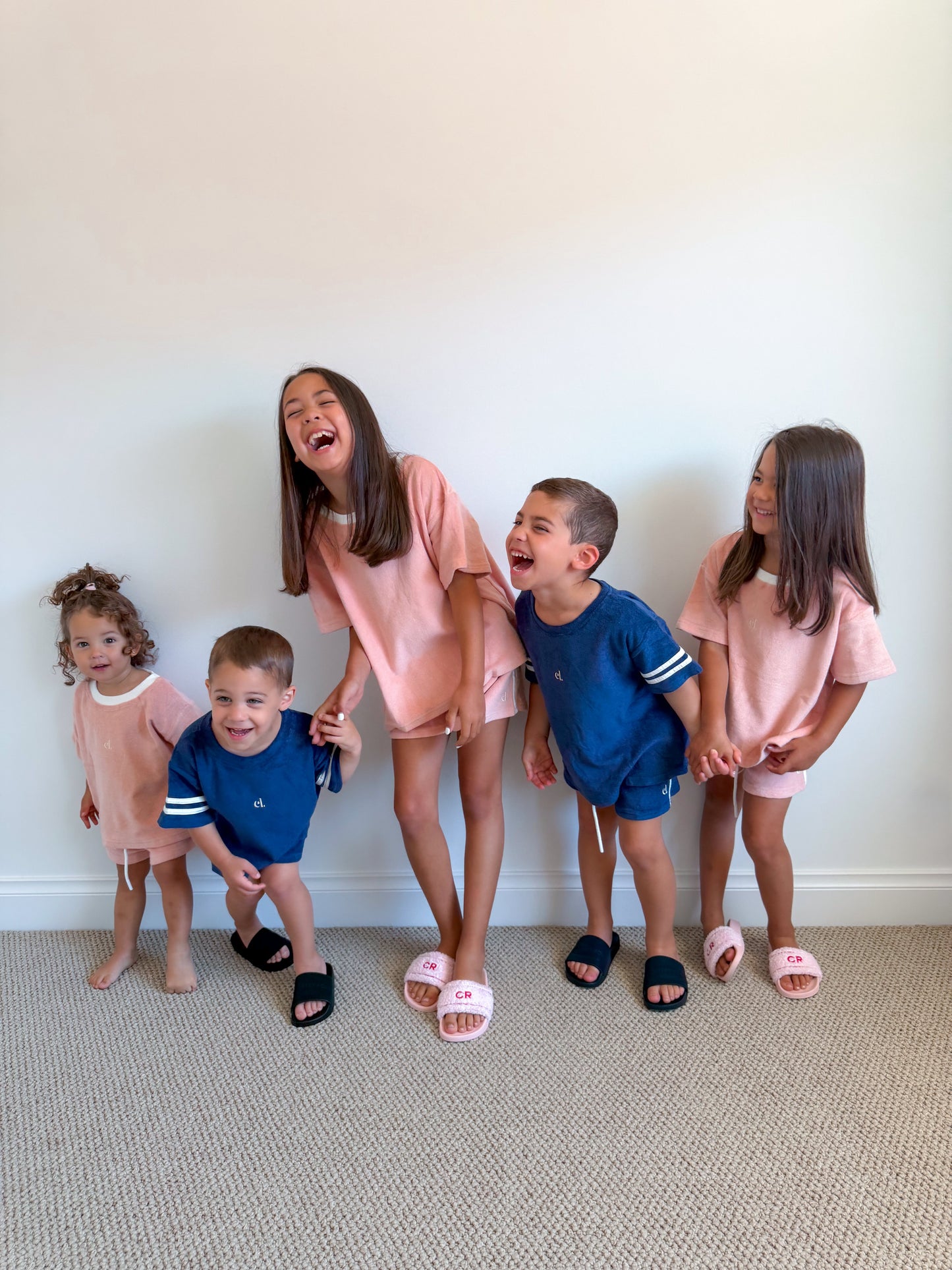 Five children in matching outfits standing against a white wall.
