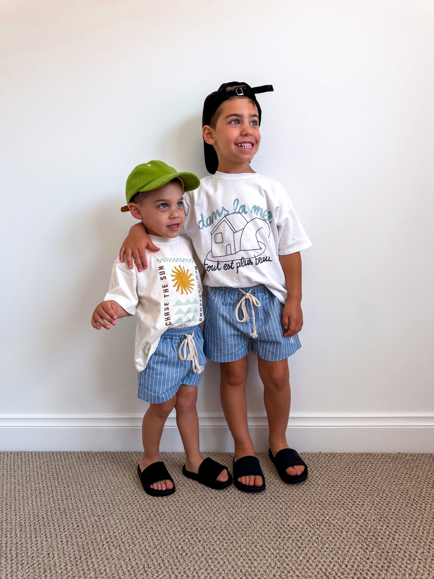 Two children wearing matching blue Cami Lane Signature Pinstripe Shorts against a white wall.