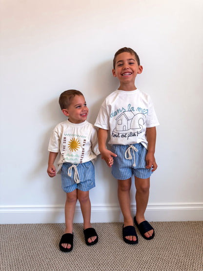 Two children wearing matching blue Cami Lane Signature Pinstripe Shorts against a white wall.