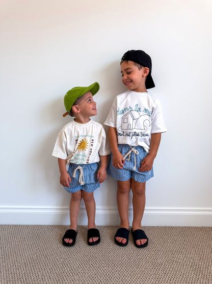 Two children wearing matching blue Cami Lane Signature Pinstripe Shorts against a white wall.