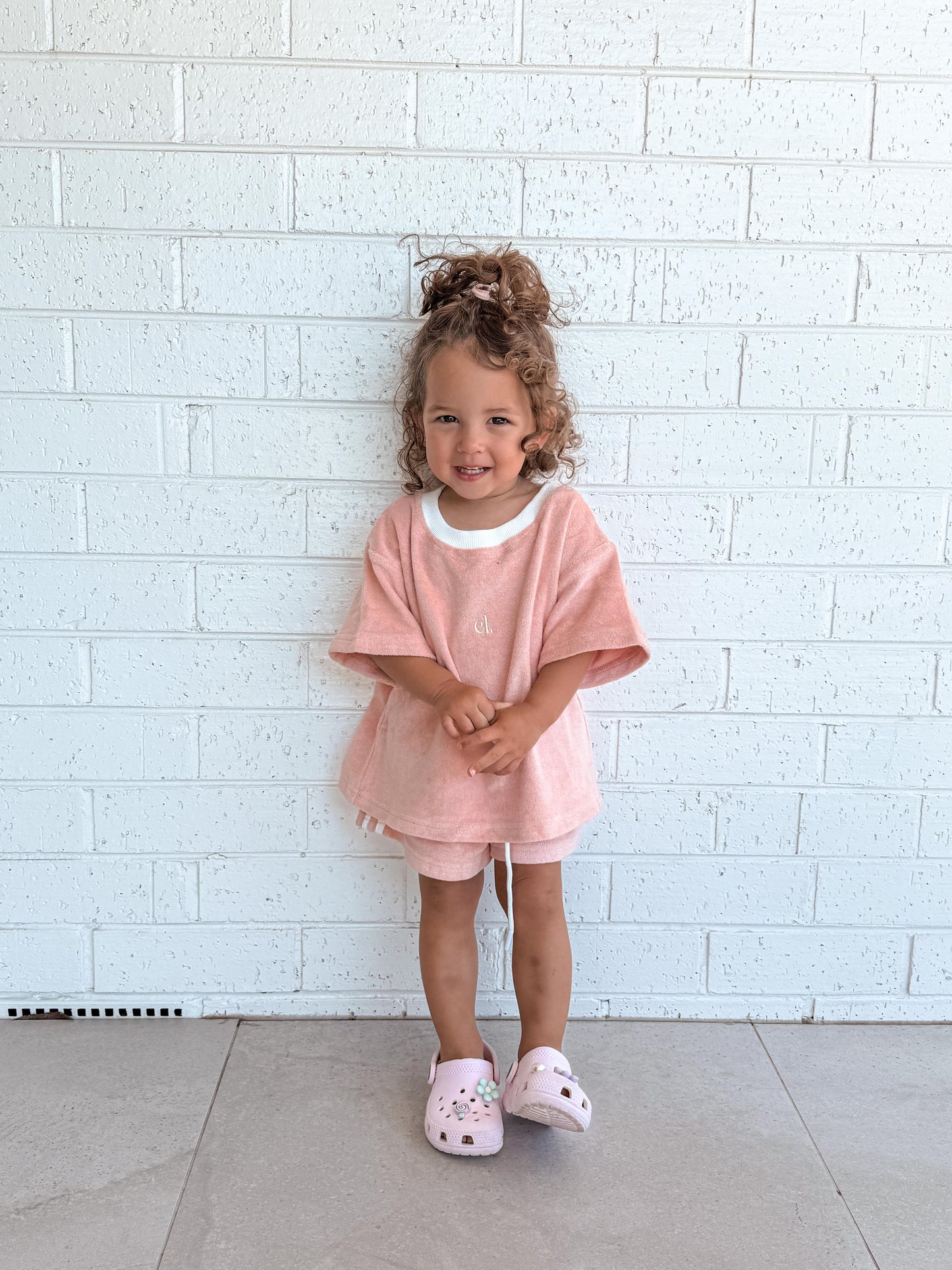 Child wearing a Cami Lane Soft Terry Set (Blush) outfit, standing against a white brick wall.