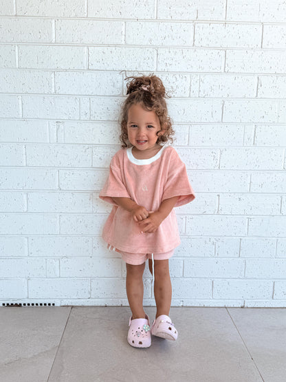 Child wearing a Cami Lane Soft Terry Set (Blush) outfit, standing against a white brick wall.